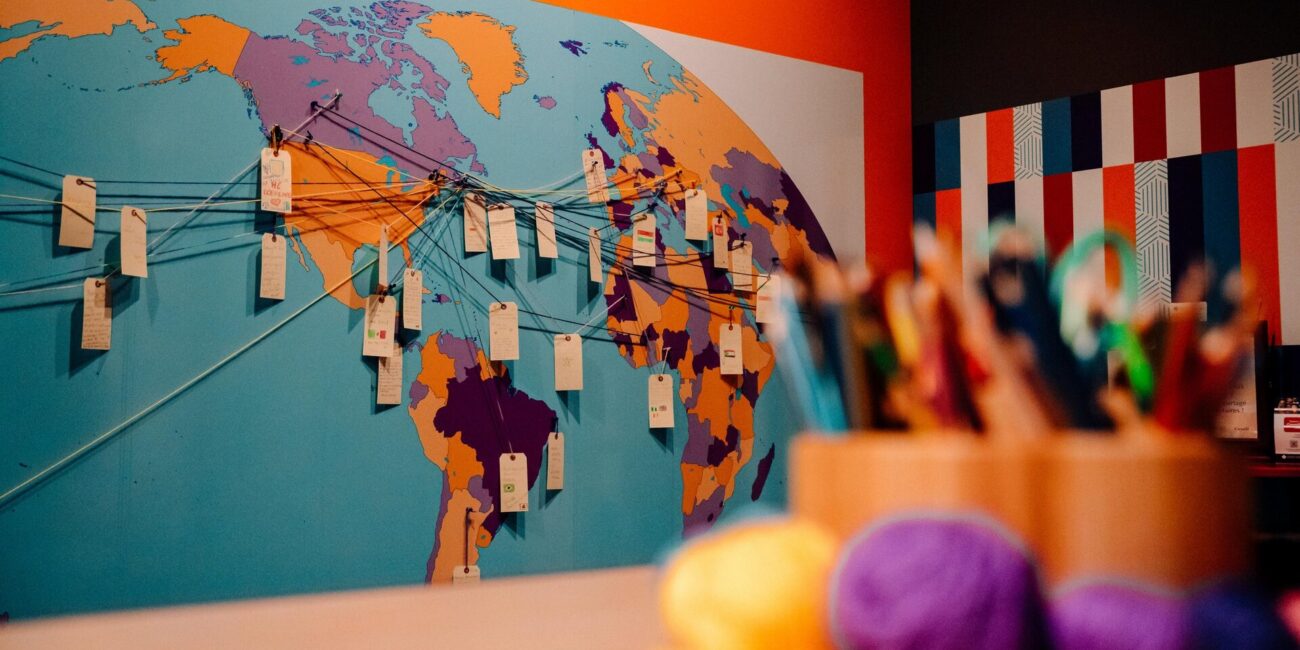 A colourful world map display at the Canadian Museum of Immigration at Pier 21, with strings connecting handwritten tags to different countries and craft supplies in the foreground.