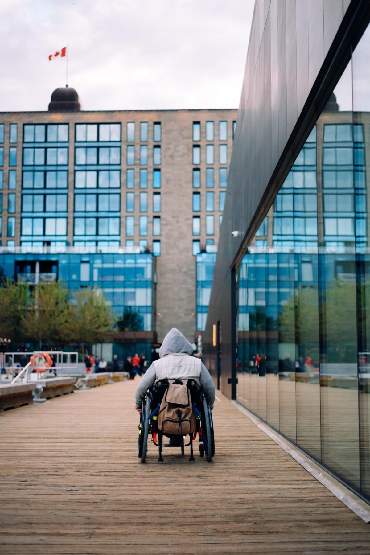 Wheelchair user travelling along the Halifax Waterfront boardwalk beside modern waterfront buildings.
