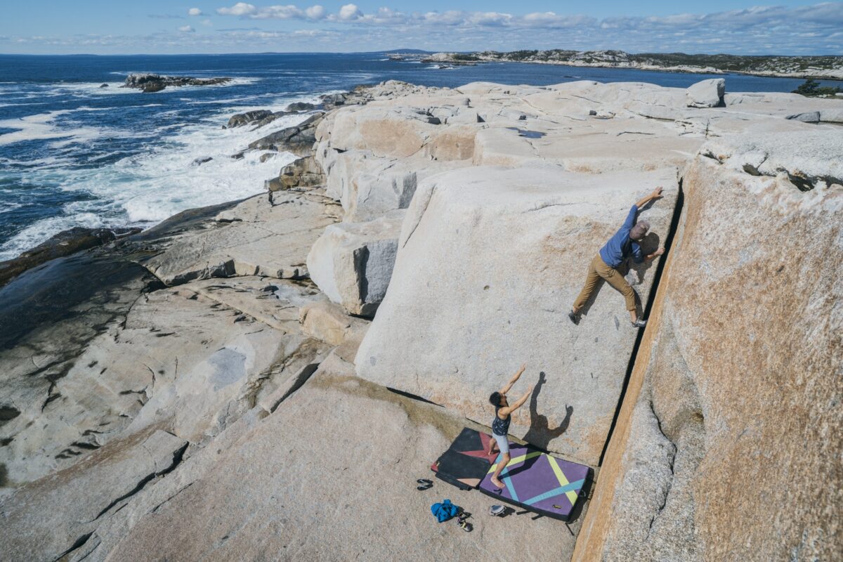 Climber bouldering on granite rock on Dover Island near Halifax, Nova Scotia, with ocean waves and rugged coastline in the background