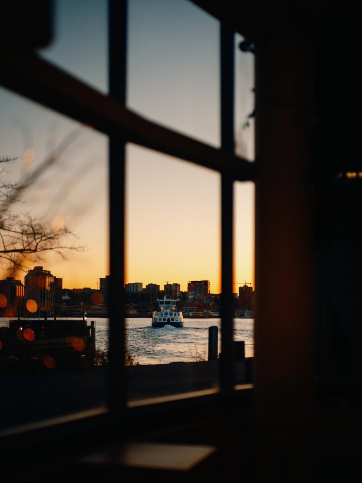 Halifax Transit ferry crossing Halifax Harbour at sunset, viewed through a window with the Downtown Halifax skyline in the background.
