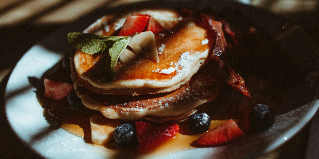 Stack of fluffy pancakes with strawberries, blueberries, syrup, and powdered sugar