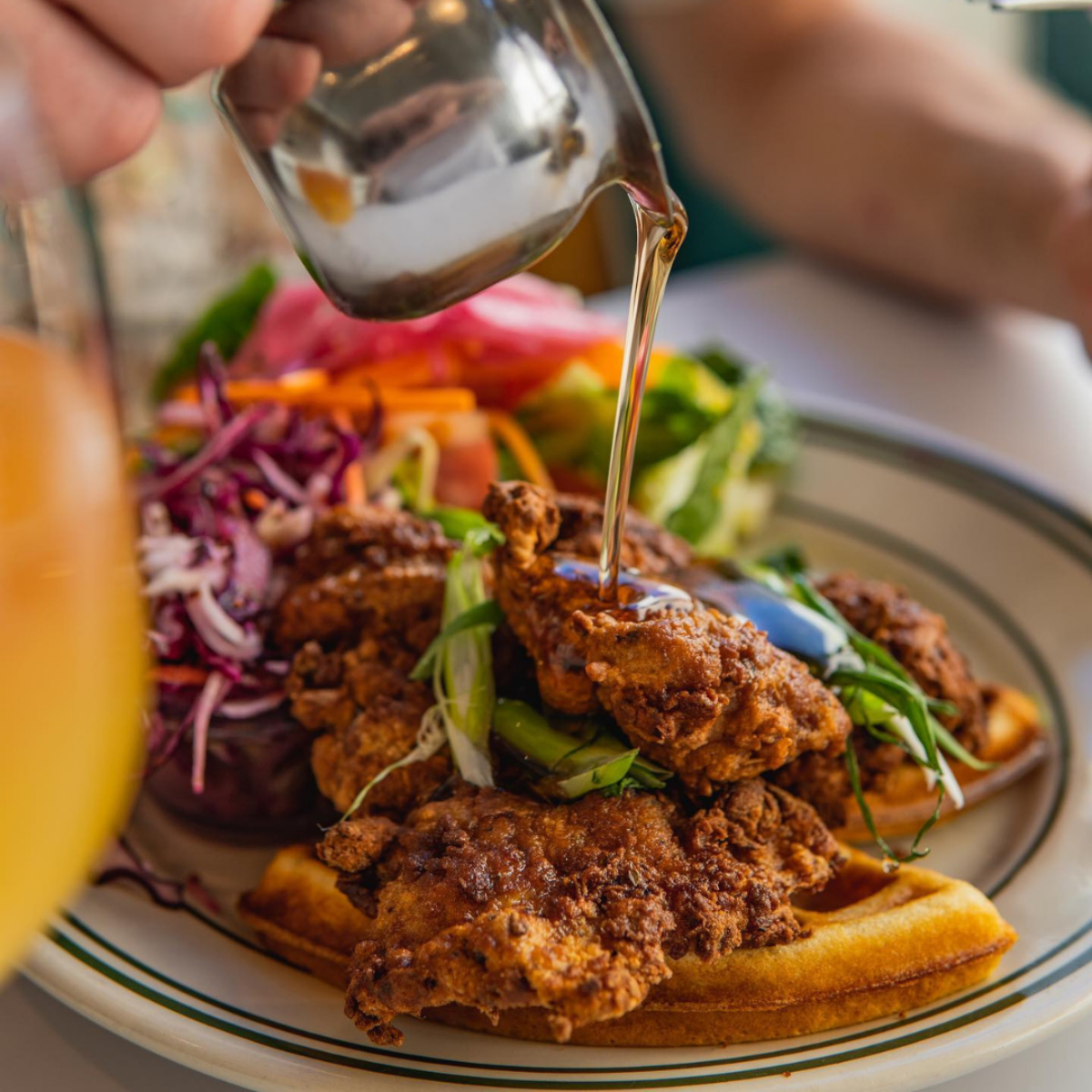 Fried chicken and waffles topped with syrup and served with fresh slaw and greens