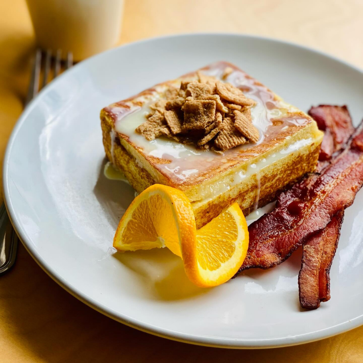 Caramelized French toast with icing, cereal topping, and crispy bacon on the side